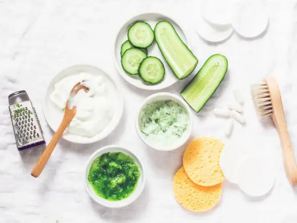 Zutaten für eine Gurkenmaske selber machen: Gurkenscheiben, Joghurt, geriebene Gurke, ein Hobel und weitere Utensilien.