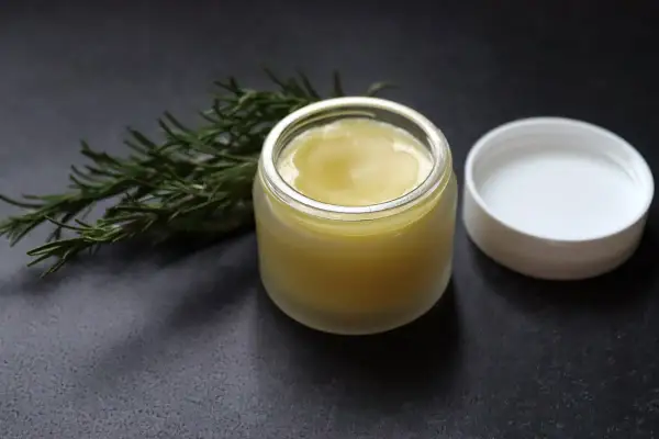 Ein Glas mit selbstgemachter Rosmarinsalbe neben einem Rosmarinzweig. Perfekt zum Rosmarin Salbe selber machen.