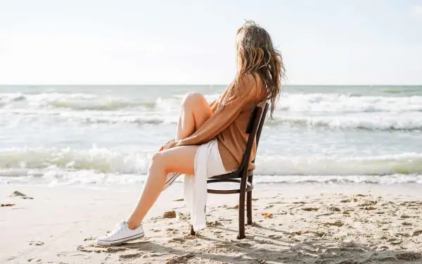 Frau sitzt am Strand auf einem Stuhl und blickt aufs Meer. Sie fragt sich, wie werde ich geduldiger, während sie die Wellen beobachtet.