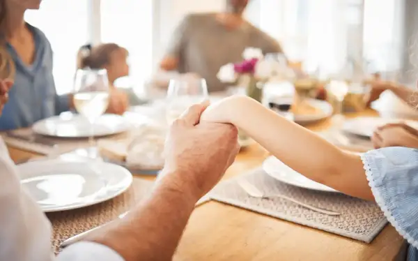 Familie hält Hände vor dem gemeinsamen Abendessen. Ein Moment des Gebets vor dem Essen.