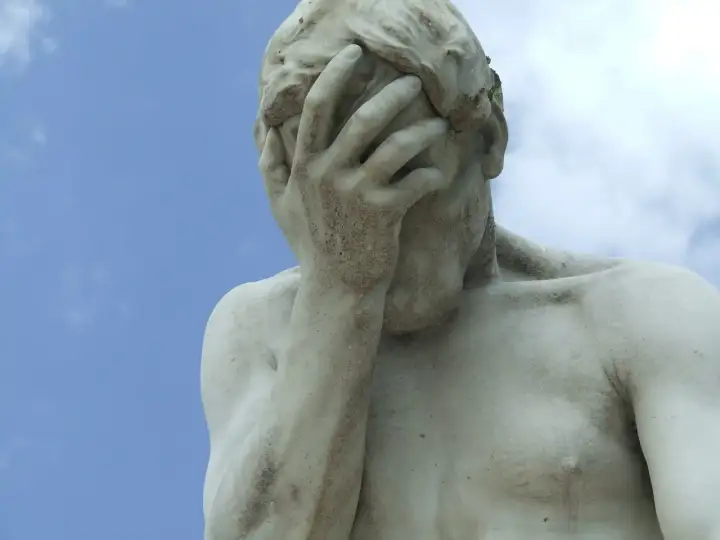 Marmorstatue mit verdecktem Gesicht im blauen Himmel. Ein Symbol für das Aushalten von Schmerzen, Tipps zur Bewältigung.